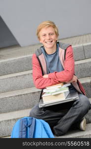 Happy student with books and laptop sitting outside on steps