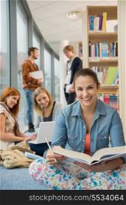 Happy student with classmates in background sitting in school library