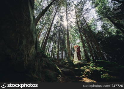 Happy stylish couple newlyweds in the green forest on summer day. bride in long white dress and groom in red suit are hugging. wedding day. Happy stylish couple newlyweds in the green forest on summer day. bride in long white dress and groom in red suit are hugging. wedding day.