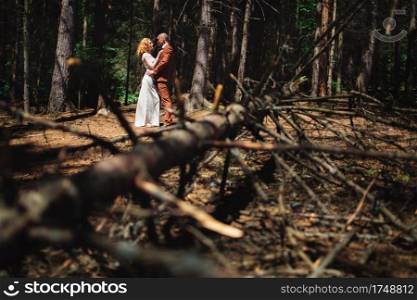 Happy stylish couple newlyweds in the green forest on summer day. bride in long white dress and groom in red suit are hugging. wedding day. Happy stylish couple newlyweds in the green forest on summer day. bride in long white dress and groom in red suit are hugging. wedding day.
