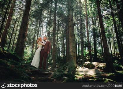 Happy stylish couple newlyweds in the green forest on summer day. bride in long white dress and groom in red suit are hugging. wedding day. Happy stylish couple newlyweds in the green forest on summer day. bride in long white dress and groom in red suit are hugging. wedding day.