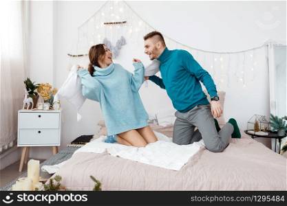 happy stylish loving couple having a pillow fight in bed. young man and woman expecting baby for Christmas. happy stylish loving couple having a pillow fight in bed. young man and woman expecting baby for Christmas. Selective focus