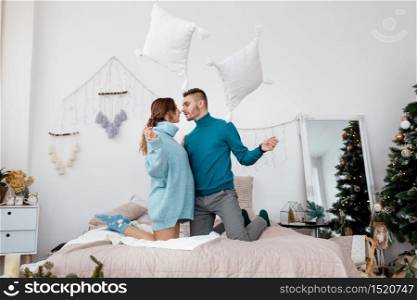 happy stylish loving couple having a pillow fight in bed. young man and woman expecting baby for Christmas. happy stylish loving couple having a pillow fight in bed. young man and woman expecting baby for Christmas. Selective focus
