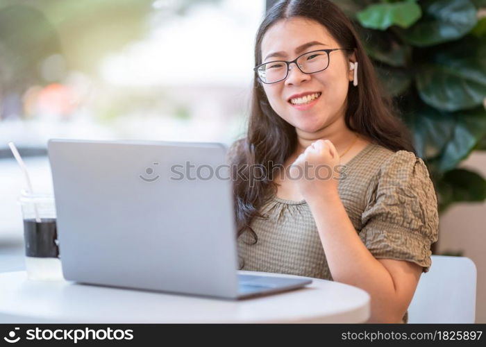 Happy successful business of asian freelance people business female wearing wireless earphonesexpressed confidence embolden working with laptop computer sitting in coffee shop like the background