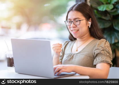 Happy successful business of asian freelance people business female wearing wireless earphonesexpressed confidence embolden working with laptop computer sitting in coffee shop like the background