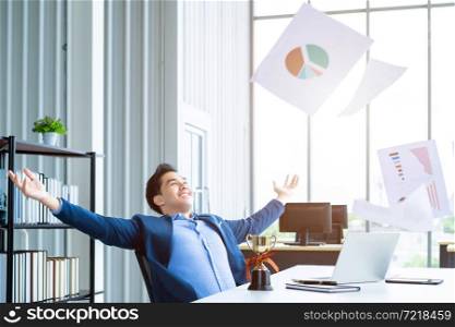 Happy successful of Asian young businessman for threw up the business plan in document paper into the air, laptop computer and a champion cup on table background in office,emotionally satisfied with