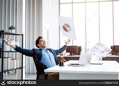 Happy successful of Asian young businessman for threw up the business plan in document paper into the air, laptop computer and a ch&ion cup on table background in office,emotionally satisfied with