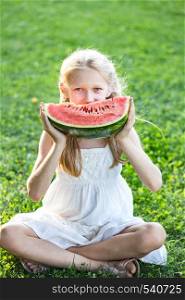 happy summer - beautiful blond little girl eating watermelon on a green lawn