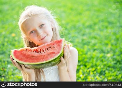 happy summer - beautiful blond little girl eating watermelon on a green lawn