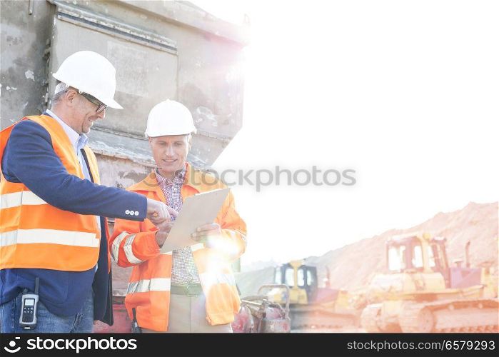Happy supervisors discussing over clipboard at construction site against clear sky