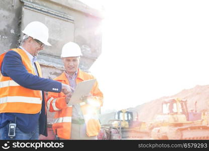 Happy supervisors discussing over clipboard at construction site against clear sky