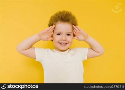 Happy surprised boy smiles and holds his hands on his head on a yellow background