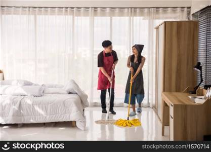 Happy sweet Asian couple cleaning bedroom floor by mop. Hygiene and health care lifestyle concept. Housework after moving to new home or apartment.
