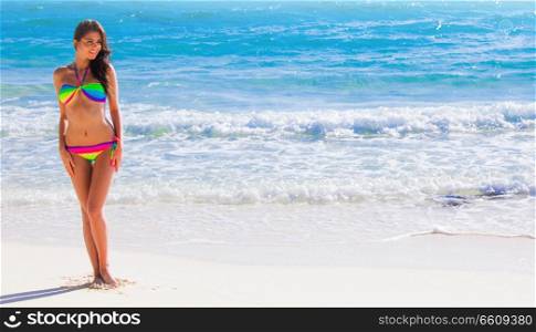 Happy tanned girl in rainbow bikini at seaside, blue sea water in background. Happy girl in bikini at seaside