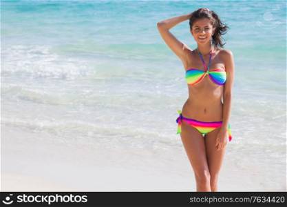 Happy tanned girl in rainbow bikini at seaside, blue sea water on background. Girl in rainbow bikini at seaside
