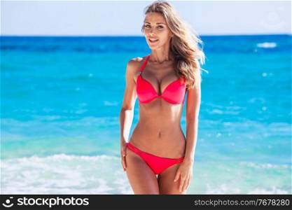 Happy tanned girl in red bikini at seaside, blue sea water in background. Happy girl in bikini at seaside
