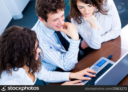 Happy team of young business people sitting in meeting room, working together on laptop computer, smiling. Overhead view.