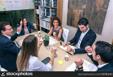 Happy teamwork celebrating business success with hands up sitting around of table in company headquarters. Teamwork celebrating business success in company headquarters