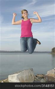 Happy teen girl jumping off large rocks at the lake.