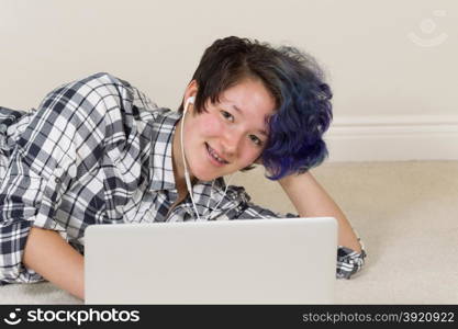 Happy teen girl, looking forward, on computer while listening to music at home.