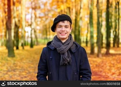 Happy teenage boy in the autumn sunny park. Happy smiling teenage boy in a beret and jacket in the autumn sunny park