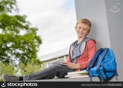 Happy teenage boy studying on wall outside his school campus
