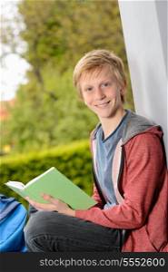 Happy teenage boy with book sitting outside on wall