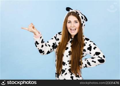 Happy teenage girl in funny nightclothes, pajamas cartoon style pointing at copy space with positive face expression, studio shot on blue. Advertisement concept. Woman wearing pajamas cartoon pointing