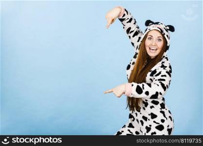 Happy teenage girl in funny nightclothes, pajamas cartoon style pointing down at copy space with positive face expression, studio shot on blue. Advertisement concept. Woman wearing pajamas cartoon pointing down