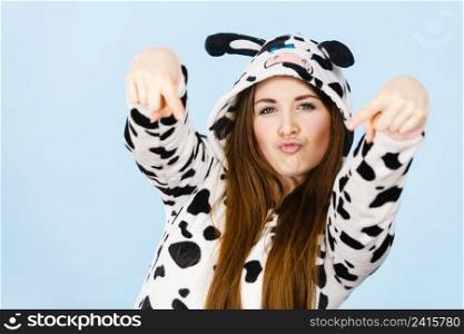 Happy teenage girl in funny nightclothes, pajamas cartoon style pointing down with positive face expression, studio shot on blue. Advertisement concept. Woman wearing pajamas cartoon pointing down
