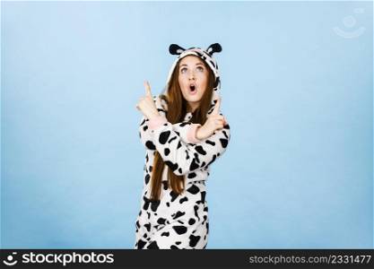 Happy teenage girl in funny nightclothes, pajamas cartoon style pointing up with positive surprised face expression, studio shot on blue. Advertisement concept. Woman wearing pajamas cartoon pointing up