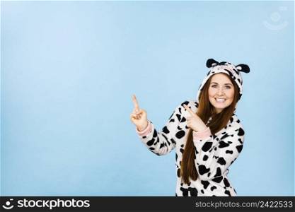 Happy teenage girl in funny nightclothes, pajamas cartoon style pointing up with positive smiling face expression, studio shot on blue. Advertisement concept. Woman wearing pajamas cartoon pointing up