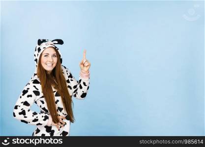 Happy teenage girl in funny nightclothes, pajamas cartoon style pointing up with positive smiling face expression, studio shot on blue. Advertisement concept. Woman wearing pajamas cartoon pointing up