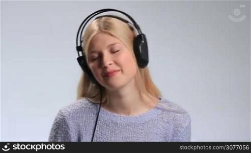 Happy teenage girl in headphones enjoying music on white. Young attractive woman with closed eyes listening to music. Cheerful female in headphones opening her eyes and blowing tender kiss into camera while relaxing and enjoying love song on radio.