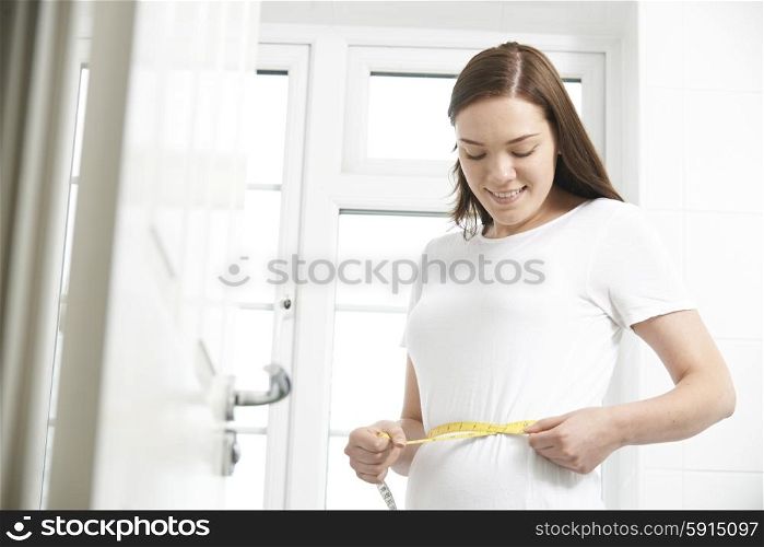 Happy Teenage Girl Measuring Waist In Bathroom