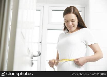 Happy Teenage Girl Measuring Waist In Bathroom