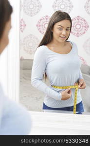 Happy Teenage Girl Measuring Waist In Mirror