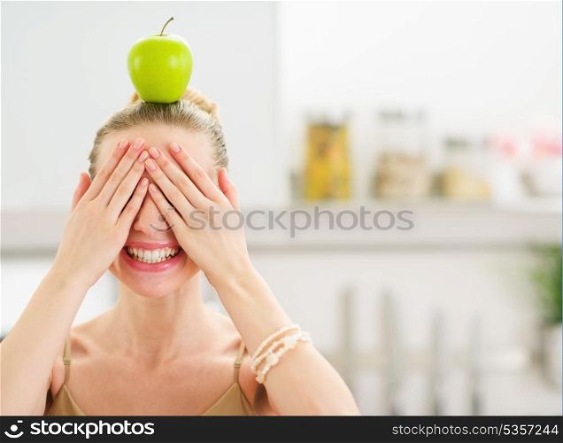 Happy teenage girl with apple on head closing eyes with hands