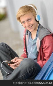 Happy teenage student listening to music wear headphones sitting outside