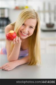Happy teenager girl eating apple in kitchen