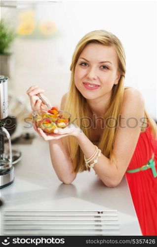 Happy teenager girl eating fresh fruits salad in kitchen
