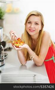 Happy teenager girl eating fresh fruits salad in kitchen