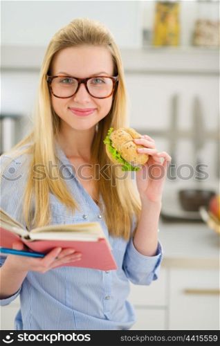 Happy teenager girl eating sandwich and reading book