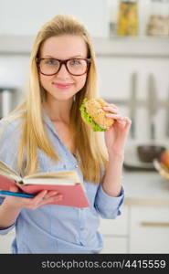 Happy teenager girl eating sandwich and reading book