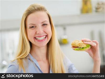 Happy teenager girl eating sandwich in kitchen