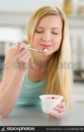 Happy teenager girl enjoying yogurt in kitchen
