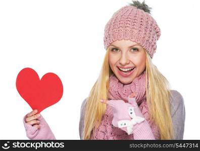 Happy teenager girl in winter hat and scarf pointing on heart shaped postcard