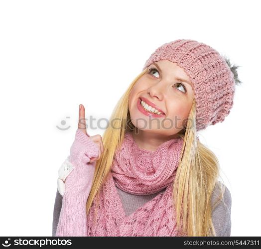 Happy teenager girl in winter hat and scarf pointing up on copy space