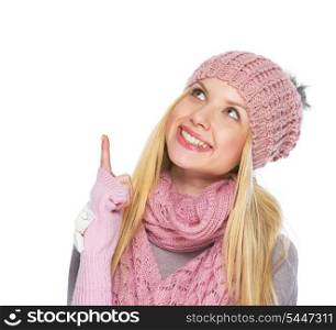 Happy teenager girl in winter hat and scarf pointing up on copy space