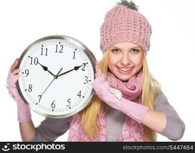 Happy teenager girl in winter hat and scarf showing clock
